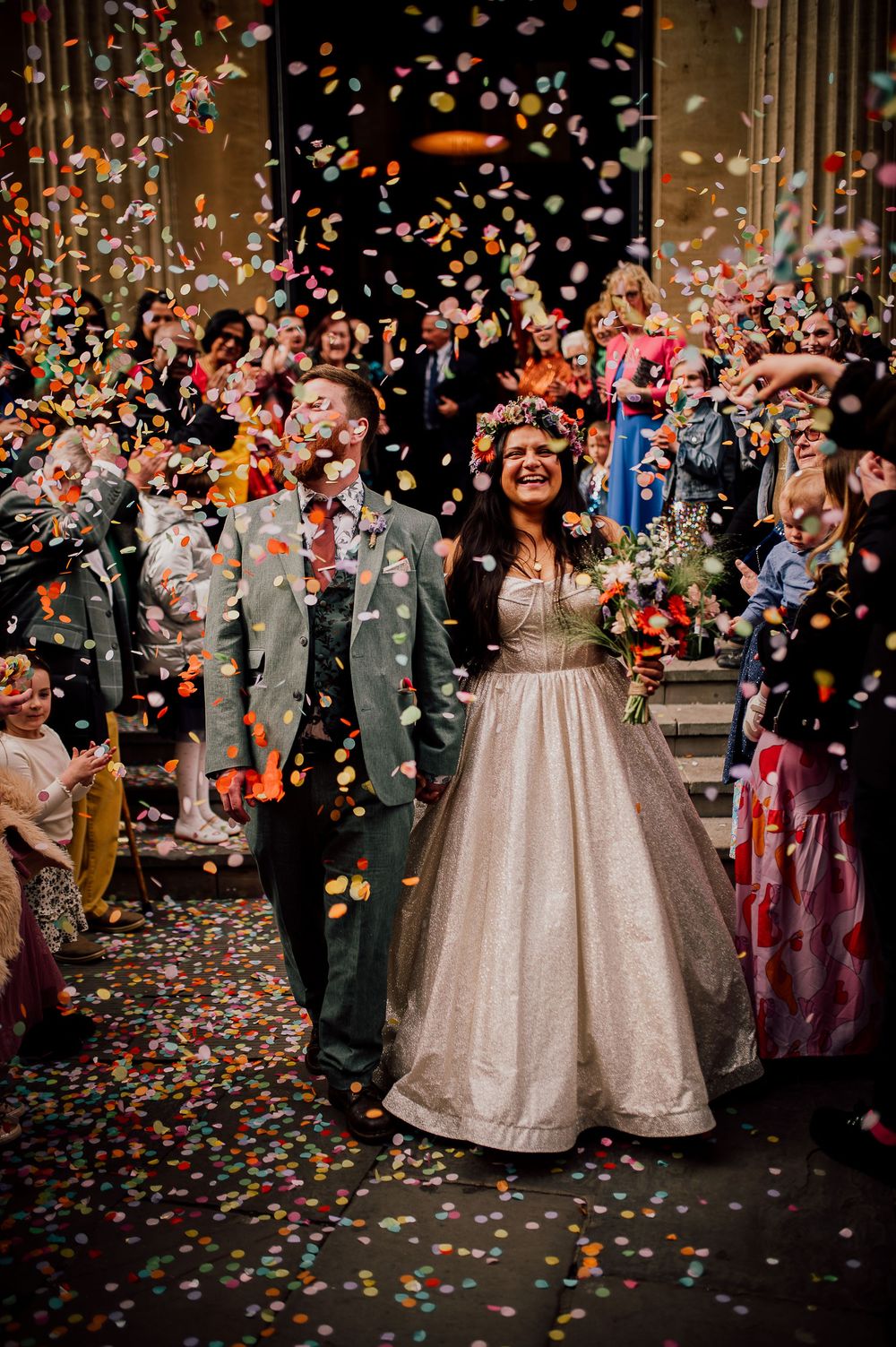 Wedding celebration with confetti being thrown at a couple in formal attire during an indoor ceremony.