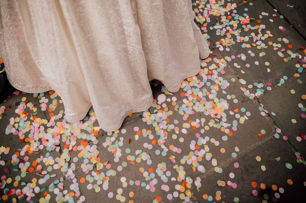 Colorful round confetti scattered across a dark floor with a light colored curtain or fabric in the background.