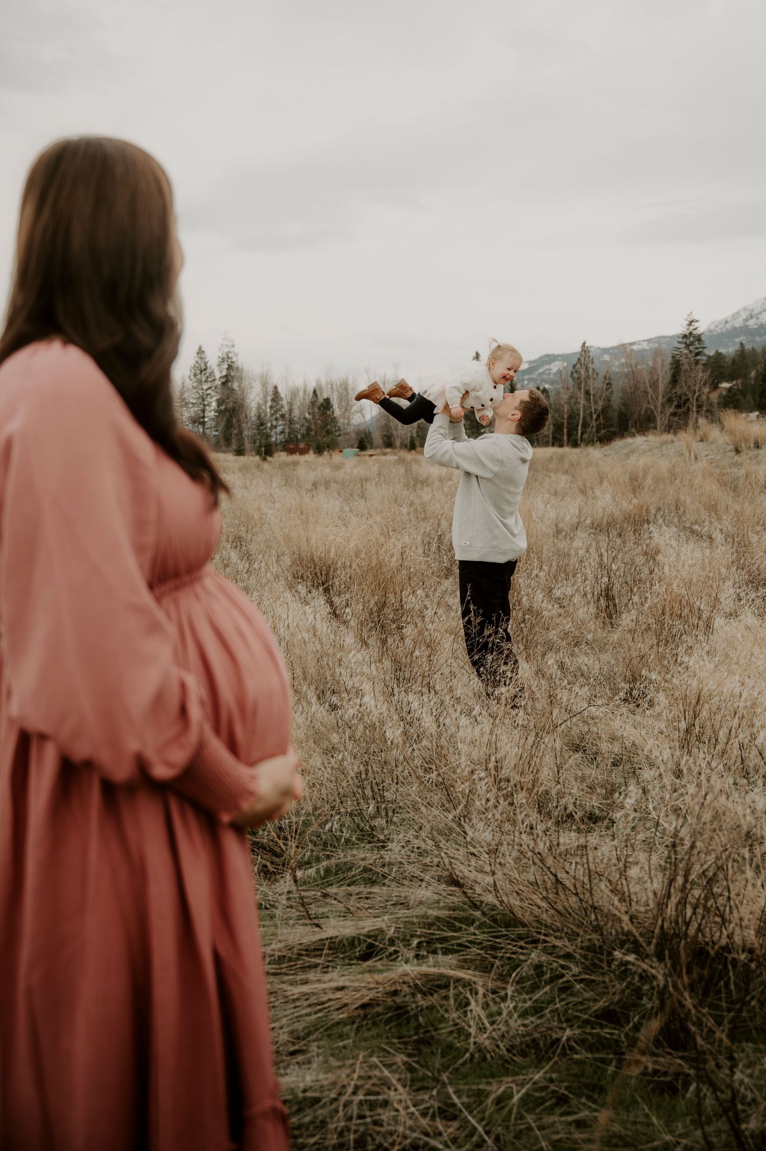 A photographer captures a moment in a rustic field with mountains and evergreen trees in the background.