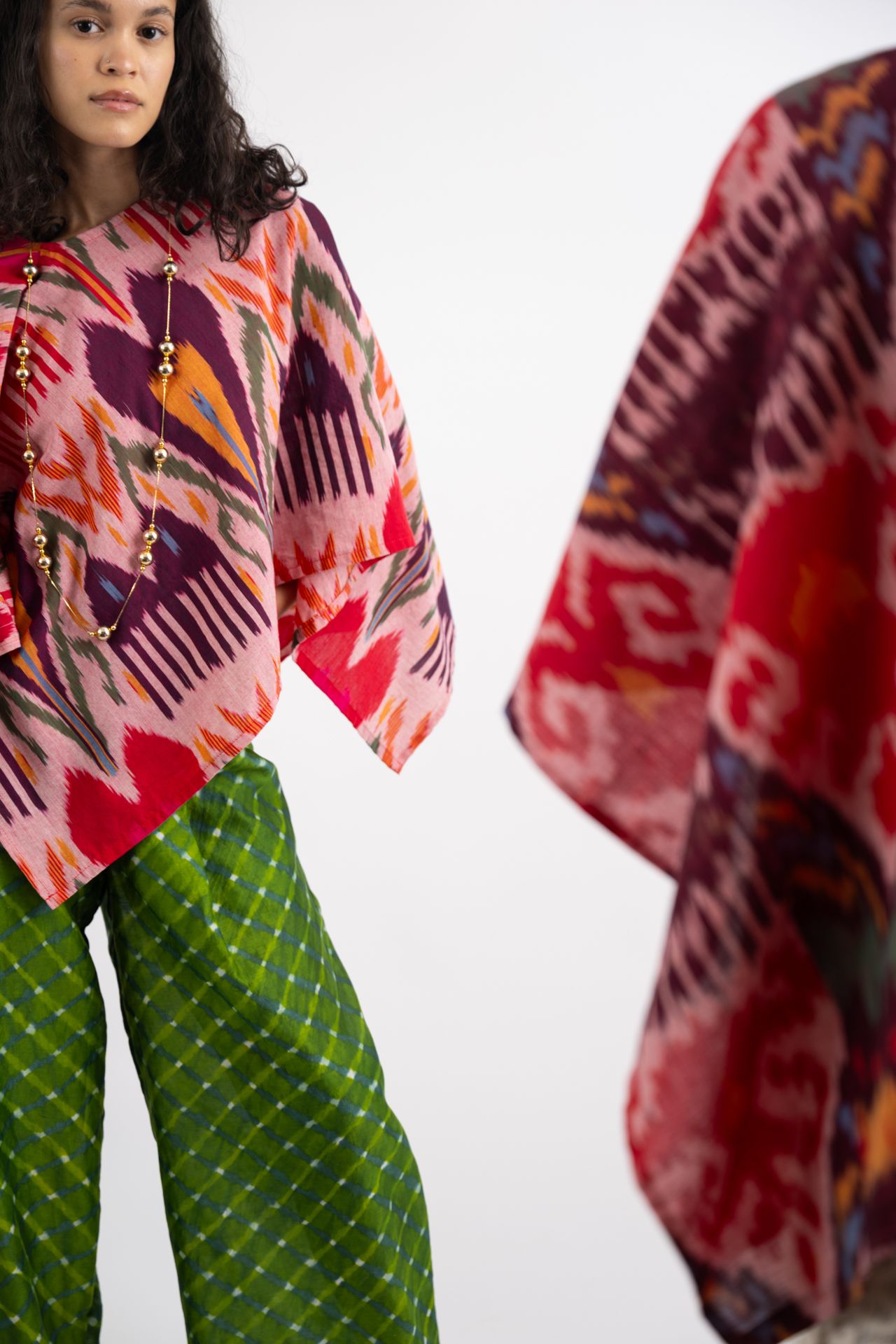 Model wearing colorful geometric print poncho top with green patterned wide-leg trousers and beige platform shoes.