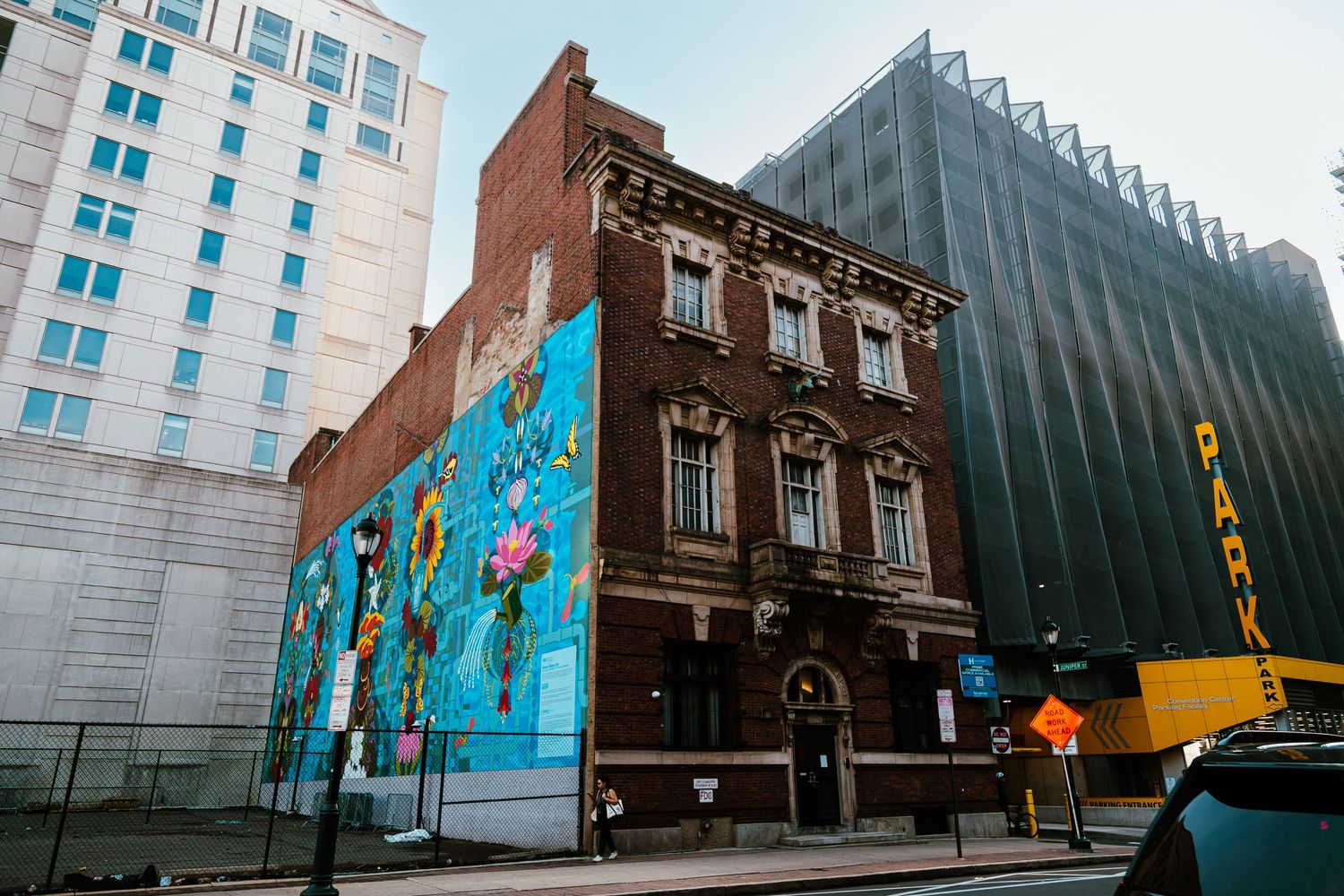 Historic brick building with vibrant floral mural on city street corner, flanked by modern skyscrapers.