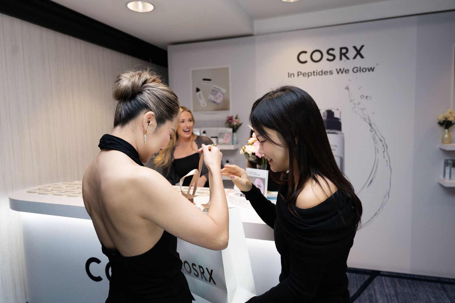 Two elegantly dressed guests pose with a COSRX sign at a Netflix and Korean Air event on a gold red carpet.