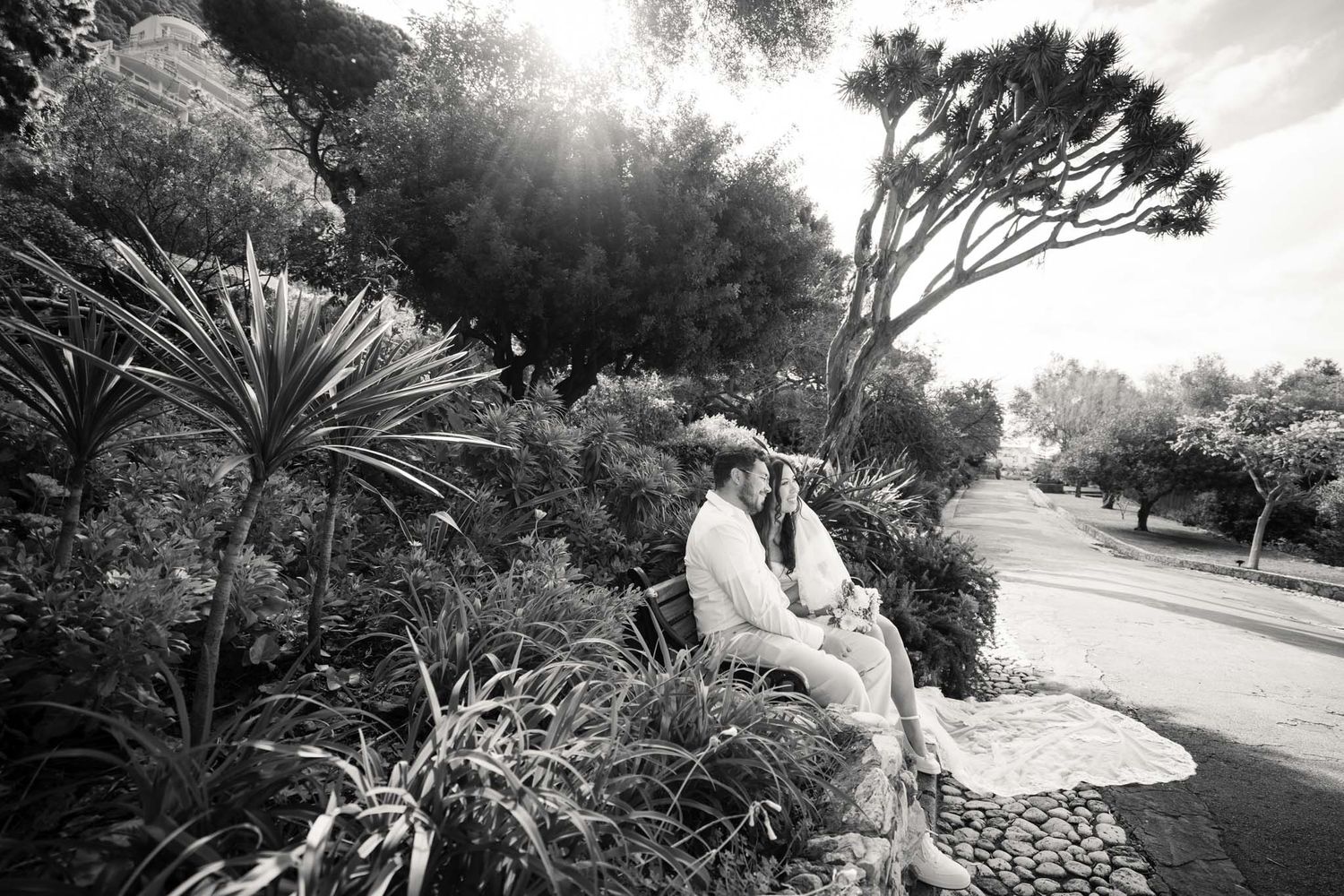 Wedding couple smile while sitting on bench in the botanical gardens, Gibraltar