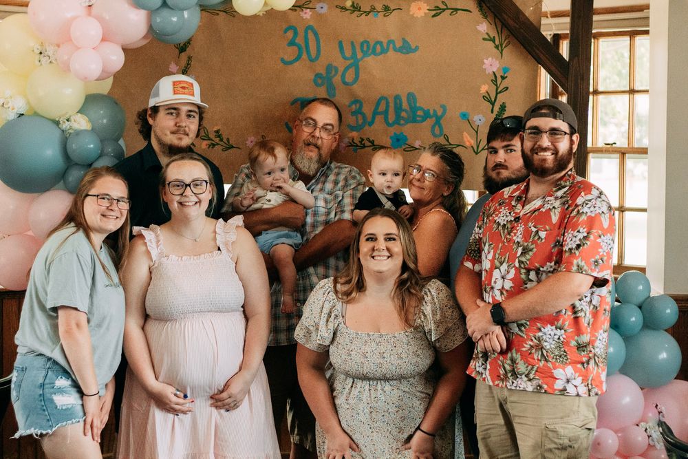 A multigenerational family group poses together indoors under a 30th anniversary balloon and banner display.