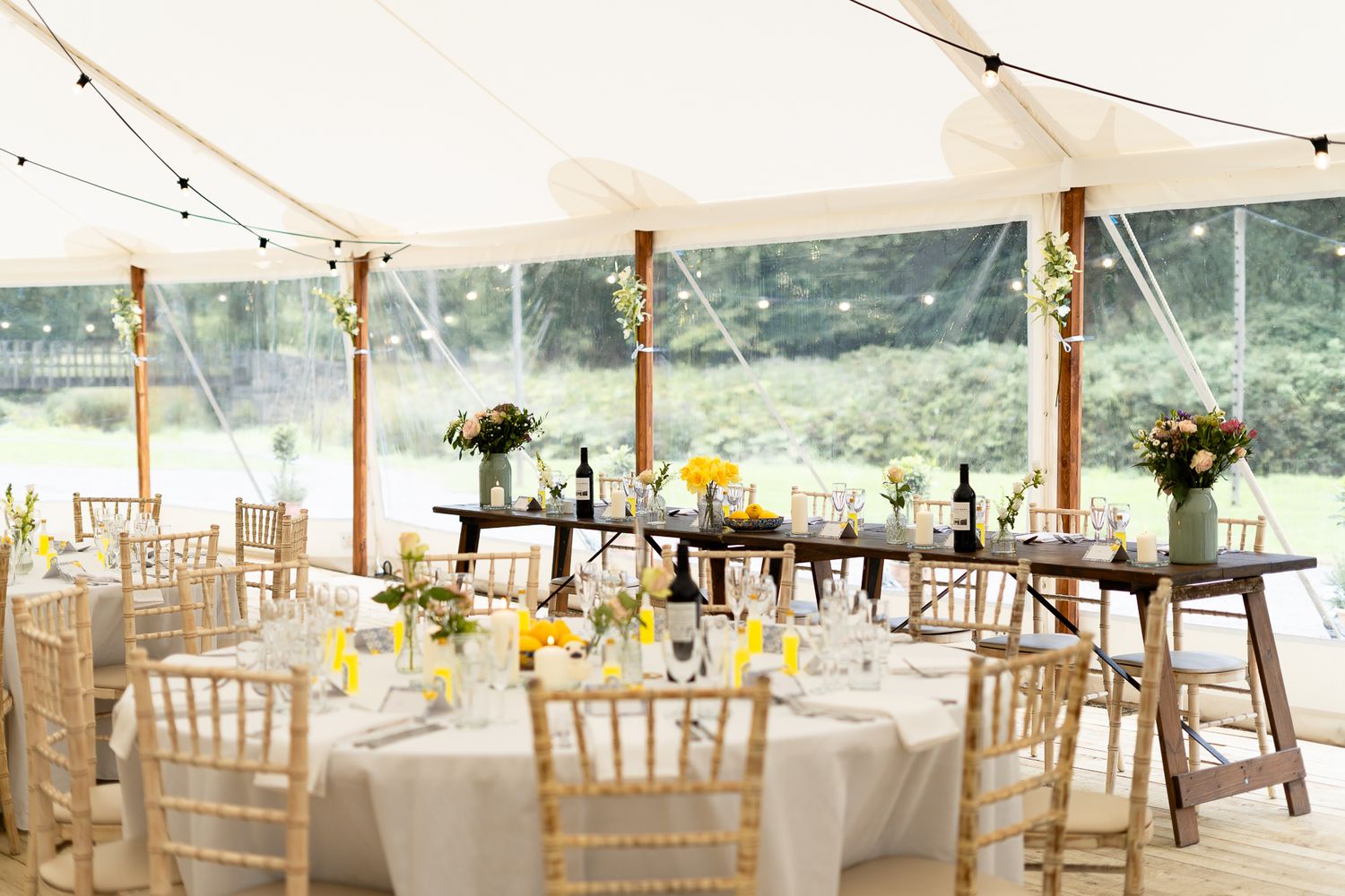 An elegant wedding reception tent with white linens, chiavari chairs and floral centerpieces.