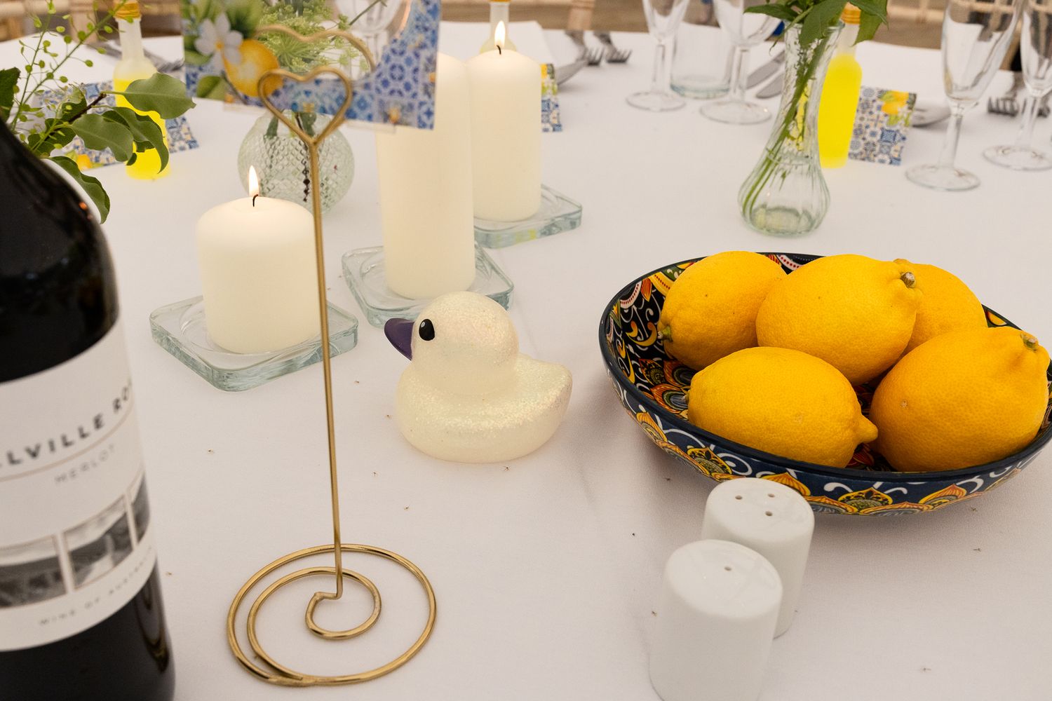 Elegant table setting with white candles, yellow lemons, and decorative plates at a formal event.