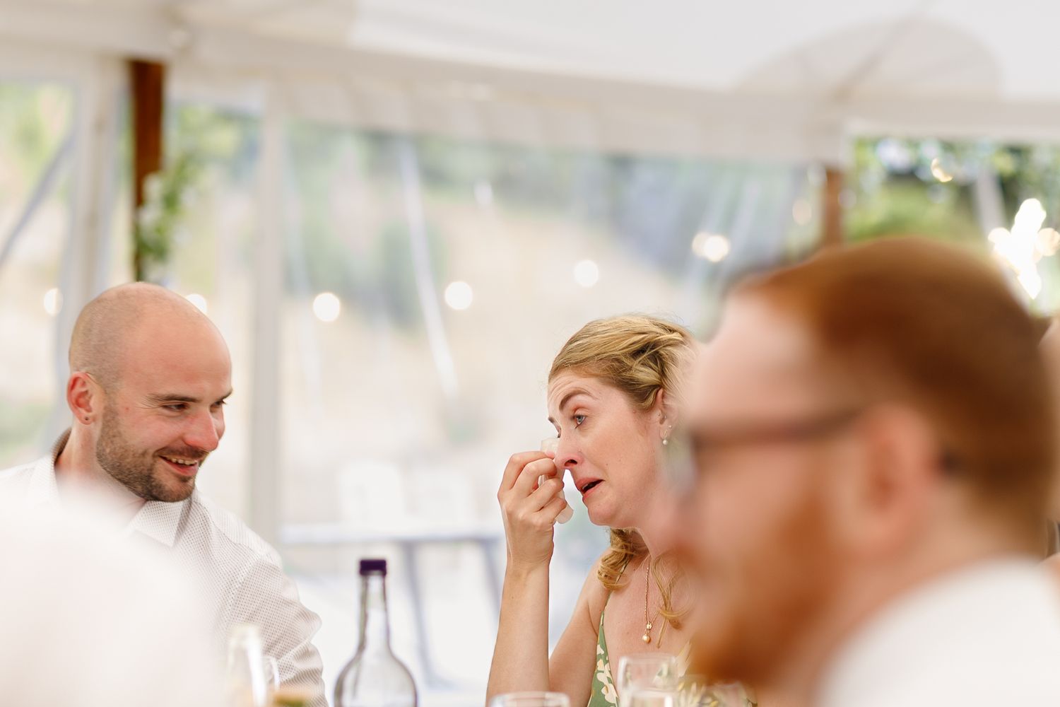 Wedding guests seated at tables during an indoor reception celebrate with raised glasses.
