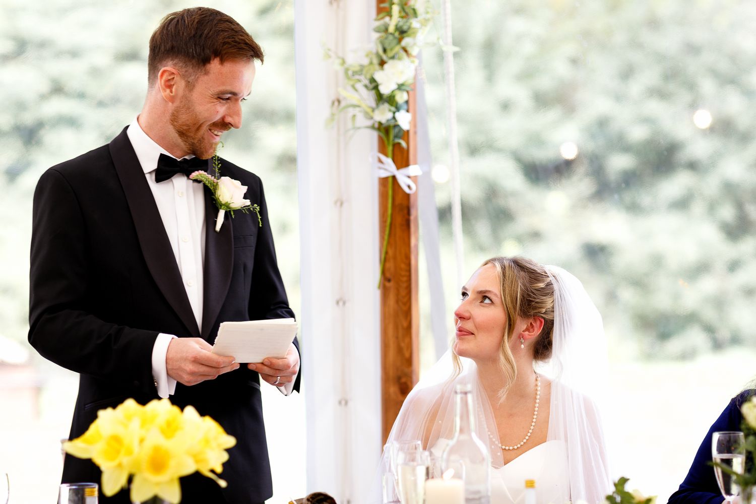 Wedding reception scene with formal attire and yellow floral decorations in an indoor venue.