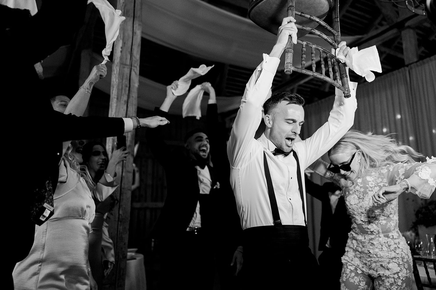 Wedding guests dancing and celebrating with raised arms at a lively black and white reception party.
