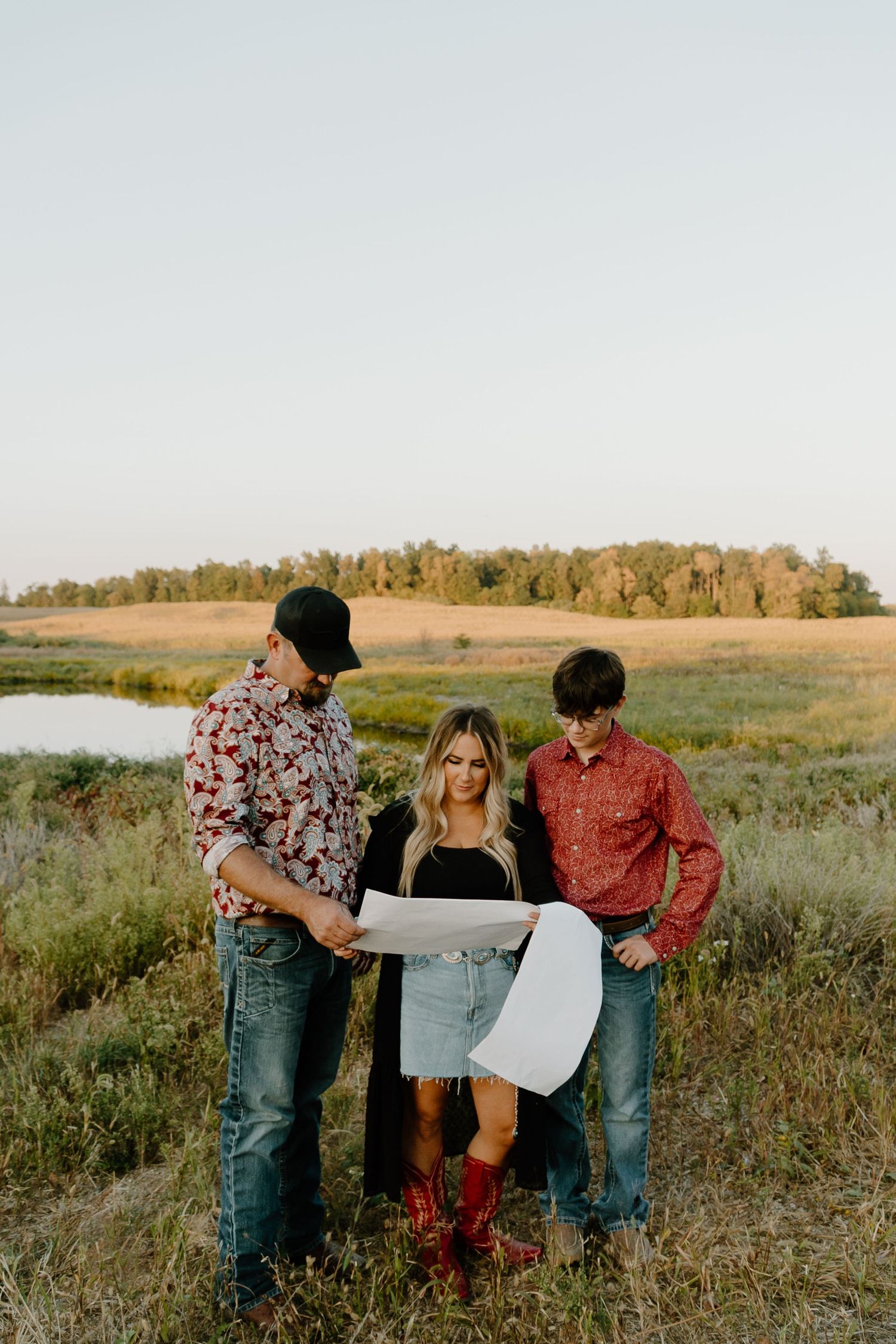 Three people look at maps together while standing in a grassy field during golden hour.