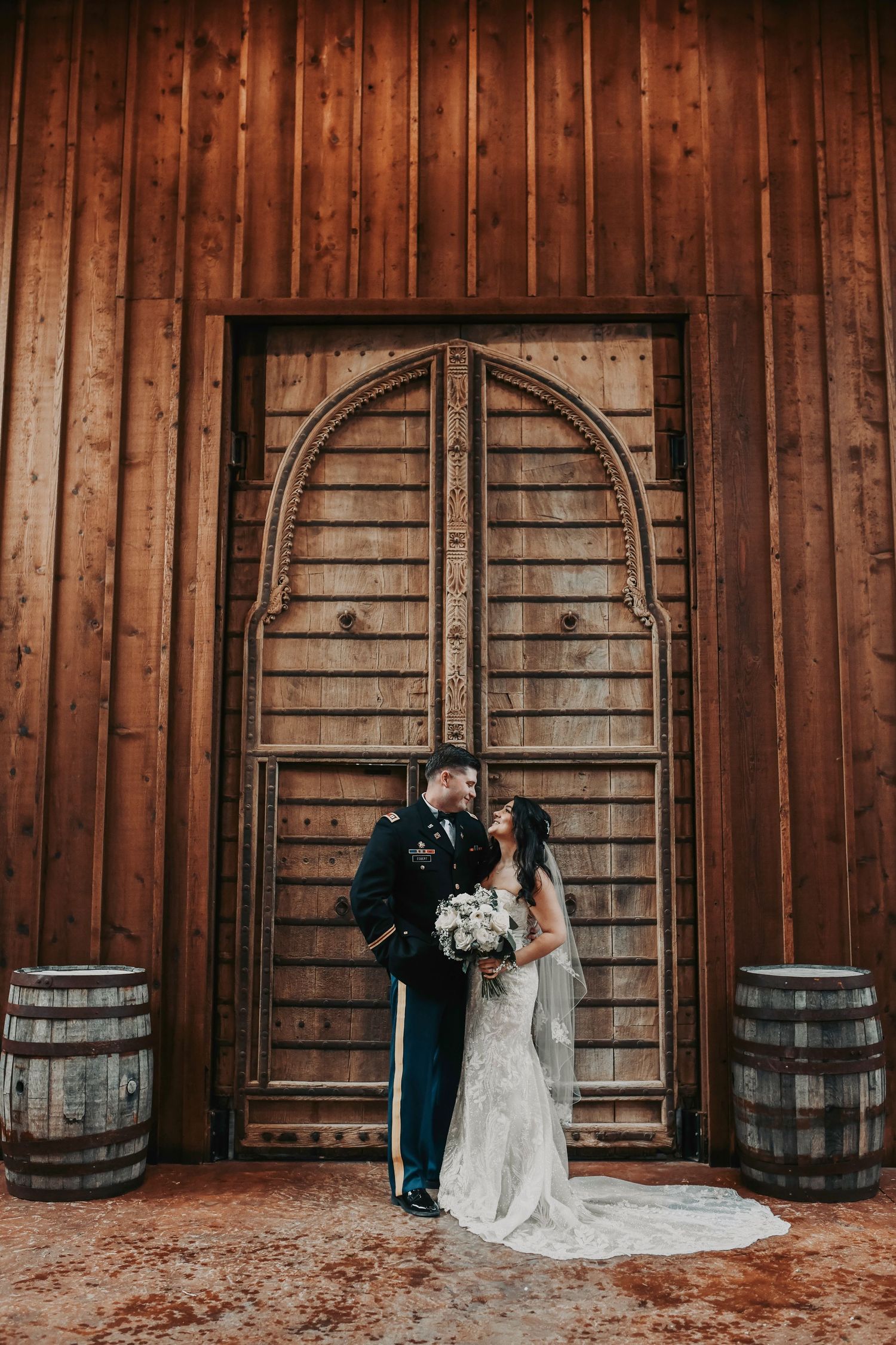 Romantic couple portrait with bride and groom posed in front of wooden barn doors.
