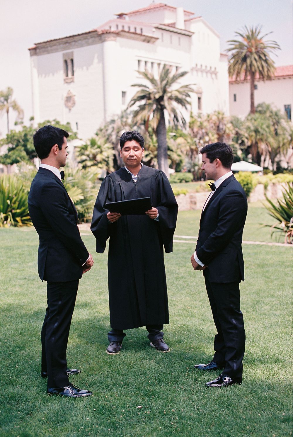 Two grooms stand on the lawn at the Santa Barbara Courthouse for their legal civil ceremony, showcasing the iconic architecture.