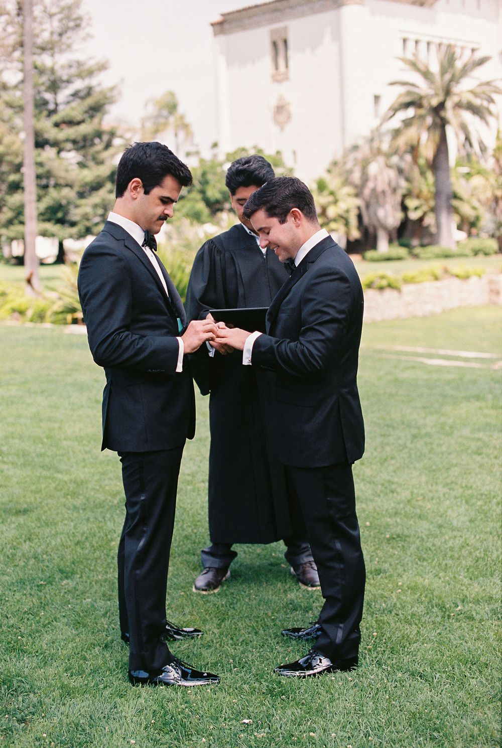 A close-up portrait of two grooms in suits exchanging rings during their Santa Barbara Courthouse elopement.