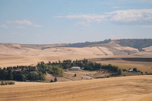 Rolling hills and farmland stretch across a golden landscape under blue skies with scattered clouds.