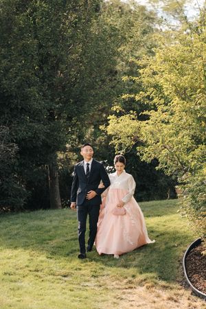 Couple strolling along garden path surrounded by lush green trees and landscaping.