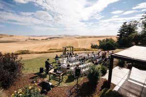 Scenic outdoor wedding venue overlooking rolling hills and golden fields under blue skies.