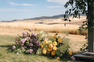 Panoramic view of rolling hills with yellow and pink floral arrangements in an outdoor wedding setting.