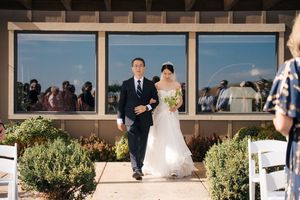 Wedding party poses outside modern venue with glass windows and greenery.