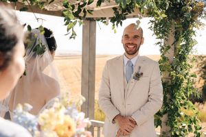 Wedding couple exchanging vows under floral arch with scenic countryside backdrop.