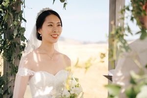 Bride poses under floral arch with scenic desert landscape in background.