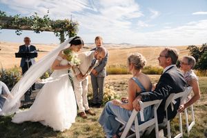Wedding guests gather on a sunny hillside for an outdoor celebration.