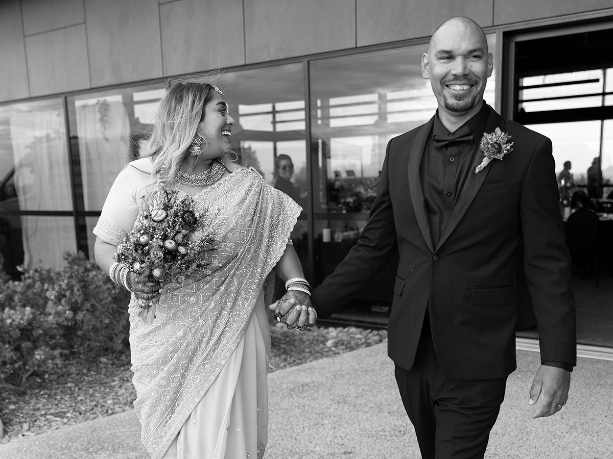 A happy couple walks together and laughs while wearing formal wedding attire on their special day.