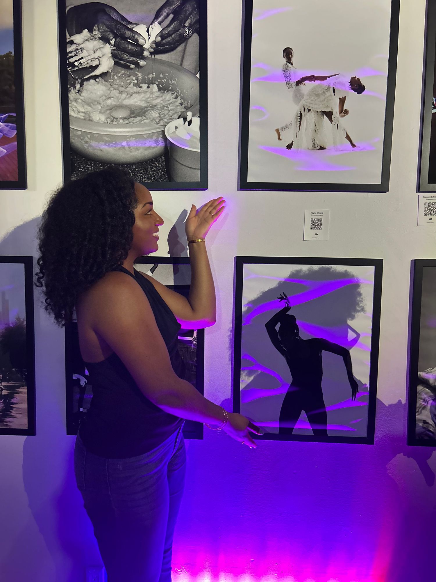 Reyna Waters stands in a gallery space with purple lighting and framed black and white photographs on the wall.