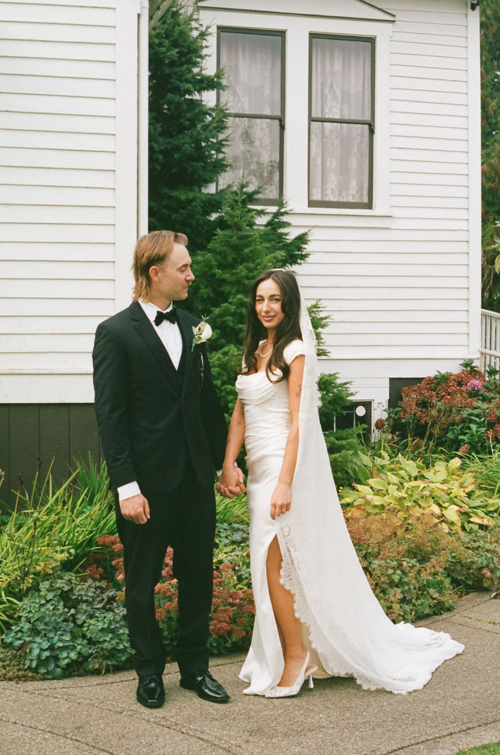 A sequence of wedding photos showing a couple in formal attire walking together on a path near a white house.