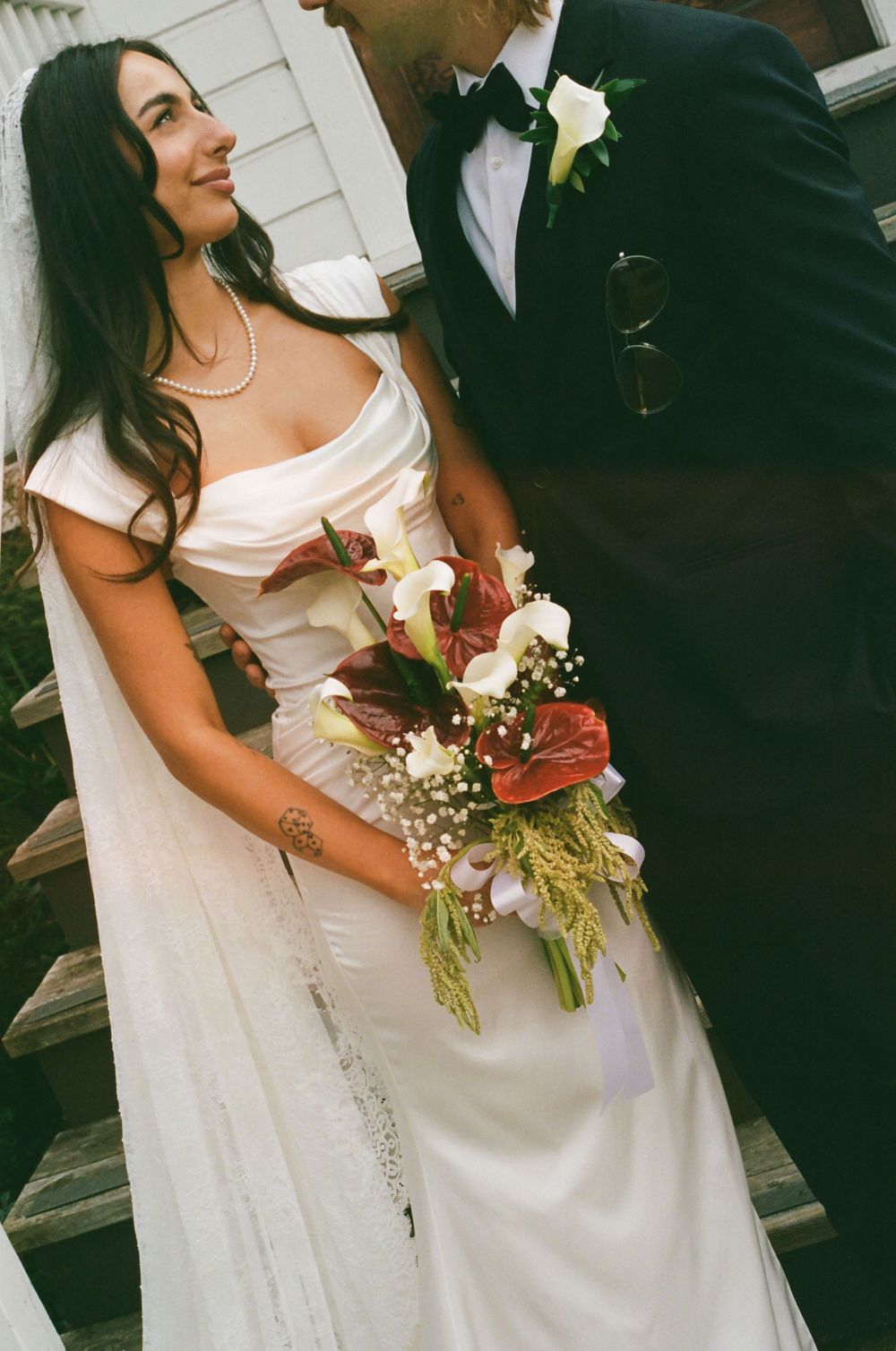 A romantic wedding moment captured with the bride holding a beautiful bouquet against a white building backdrop.