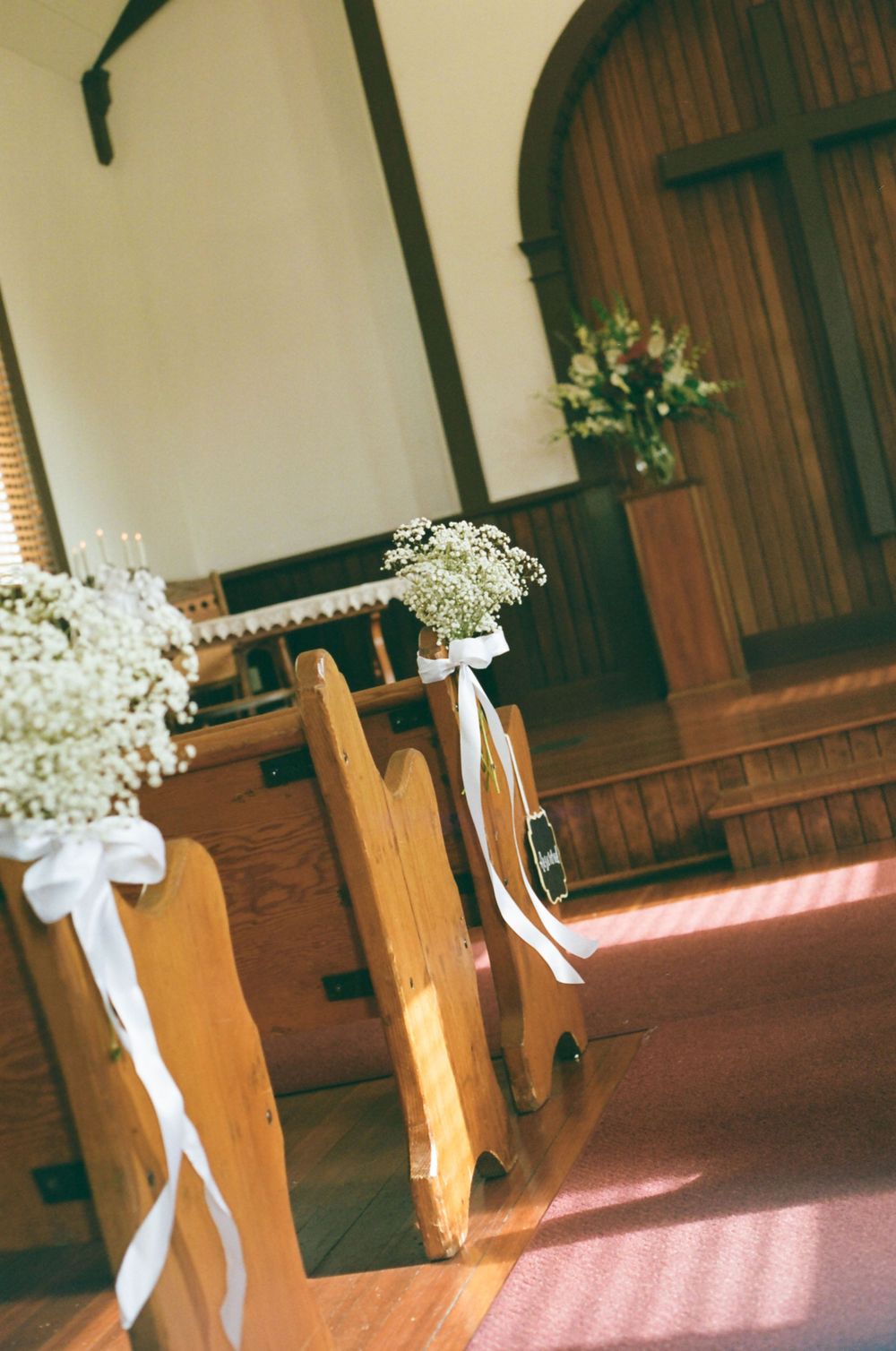 Wooden church pews decorated with baby's breath flowers and white ribbons in sunlit chapel interior.