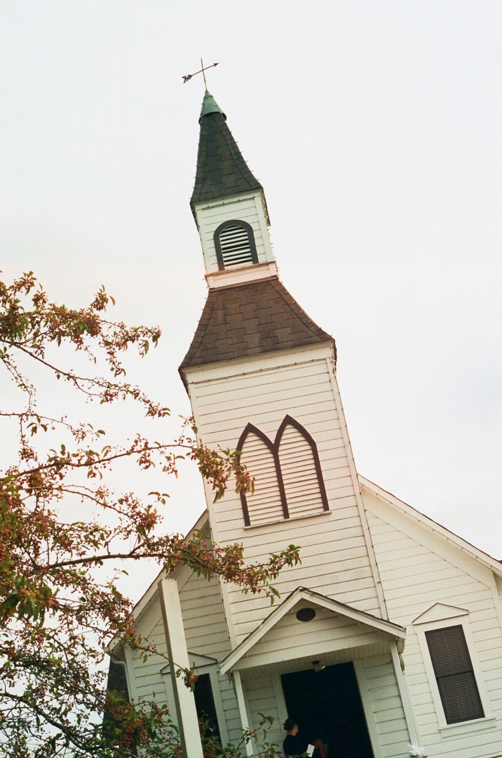 A white country church with a steeple photographed from a low angle against a bright sky.