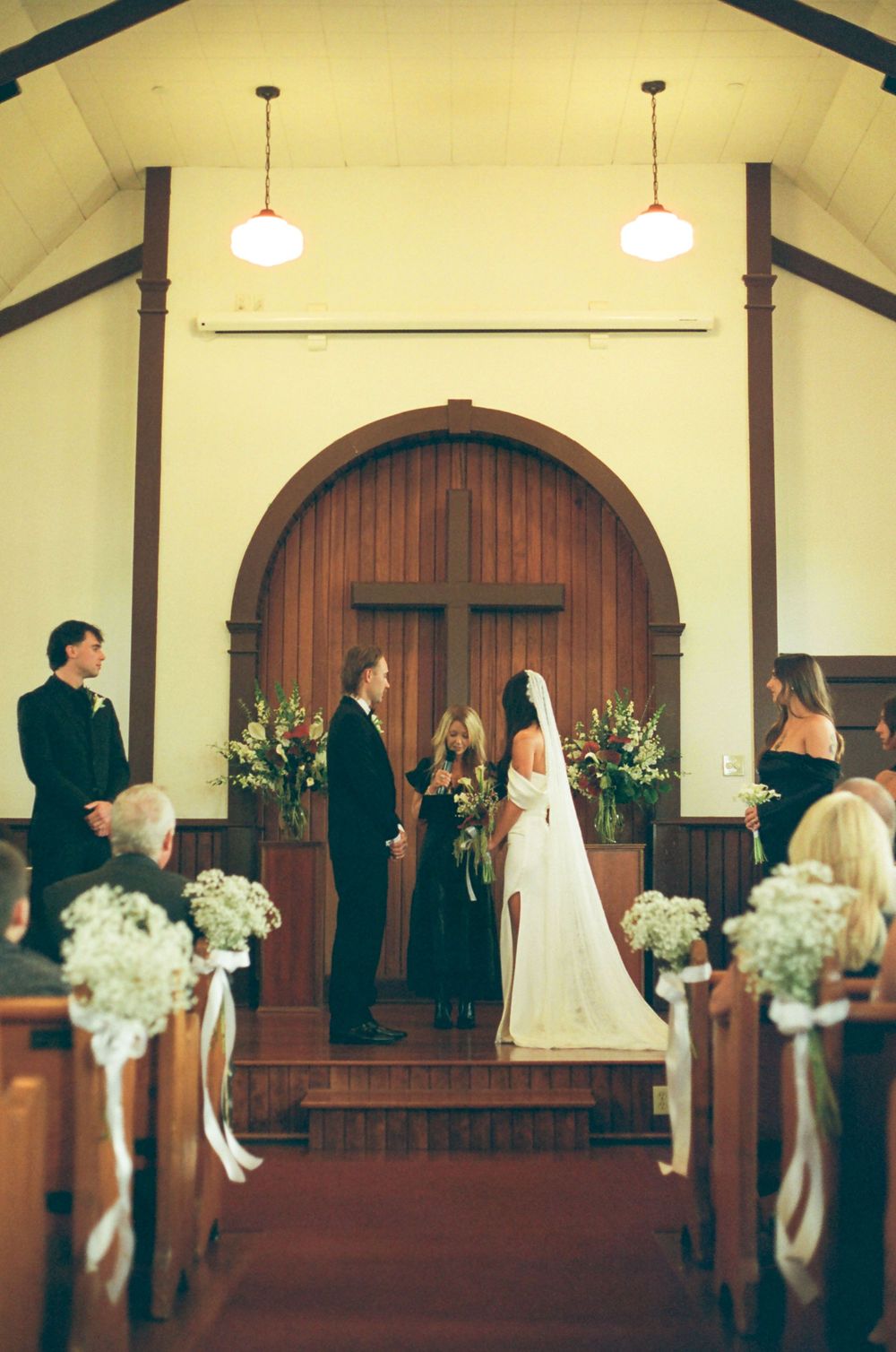 Traditional church wedding ceremony with wooden arched doors and floral arrangements lining the aisle.