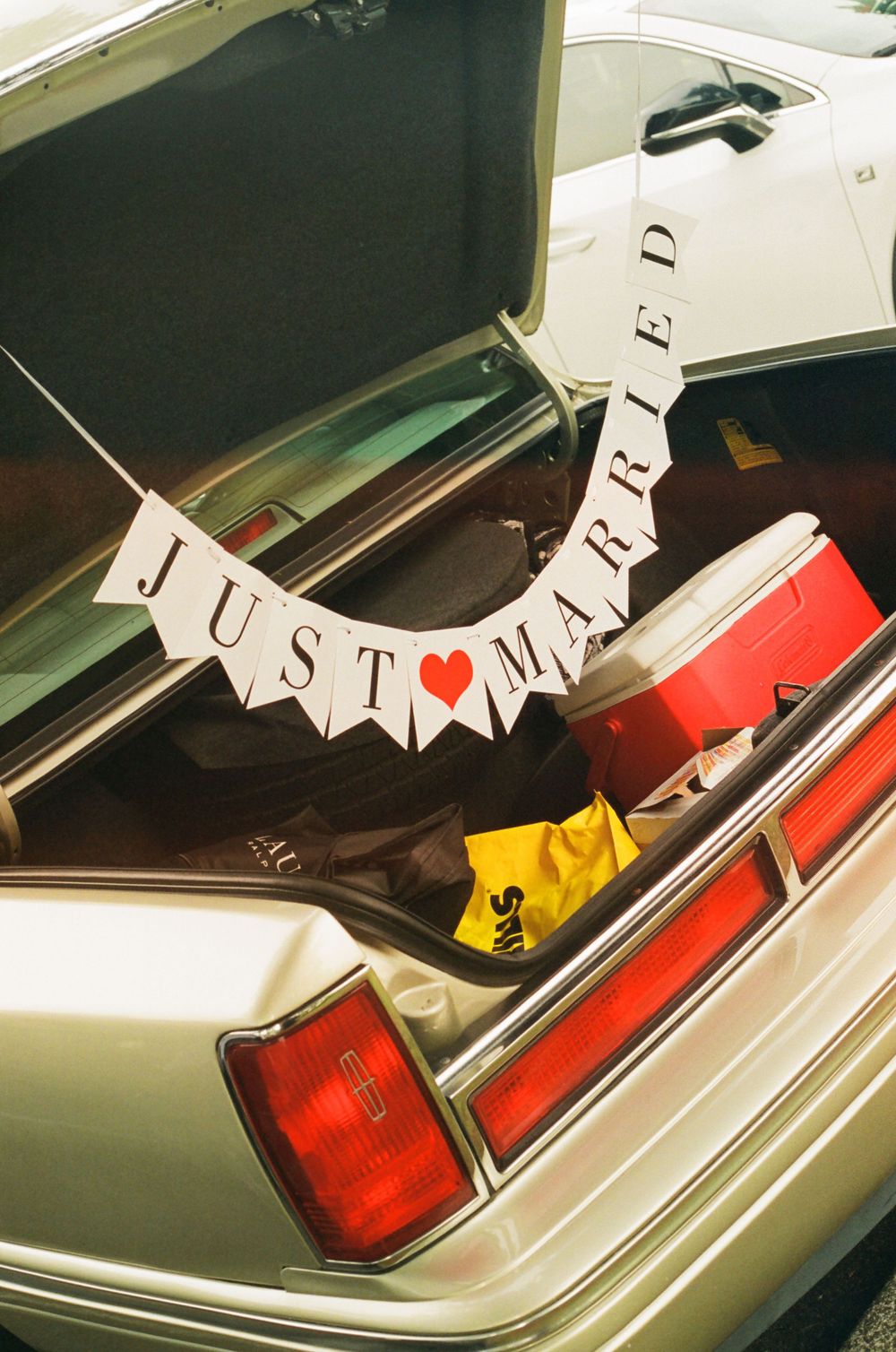 Just married banner decorates the back of a vintage car with red taillights.