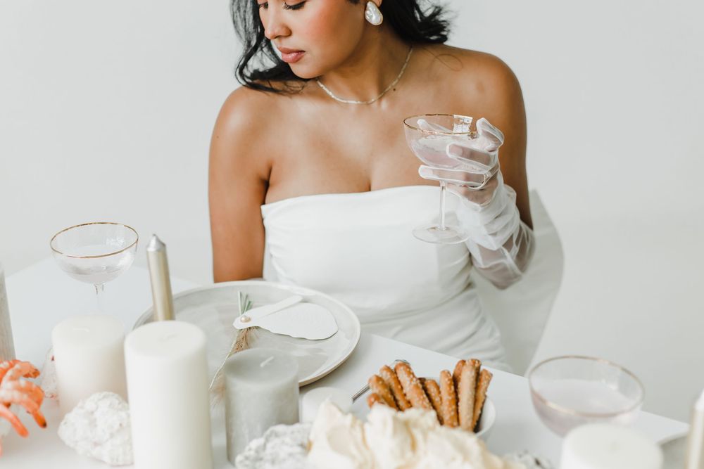 A person in a white dress arranges delicate teacups and saucers on a light-colored table setting.