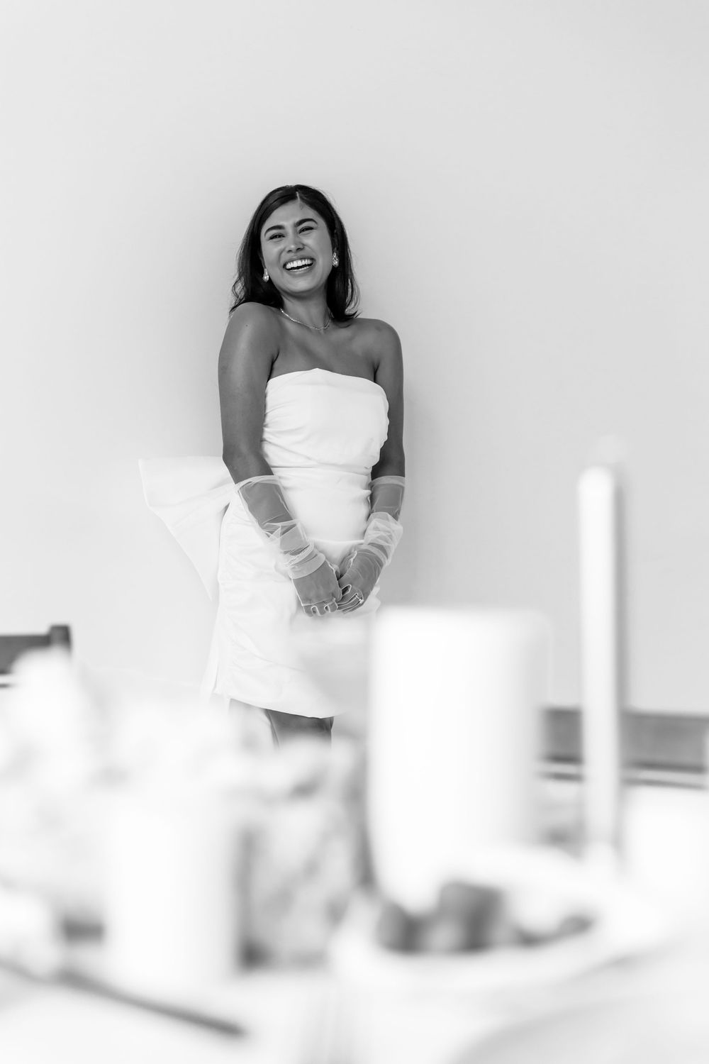 Woman in white dress laughing joyfully against minimalist white background during creative photo session.