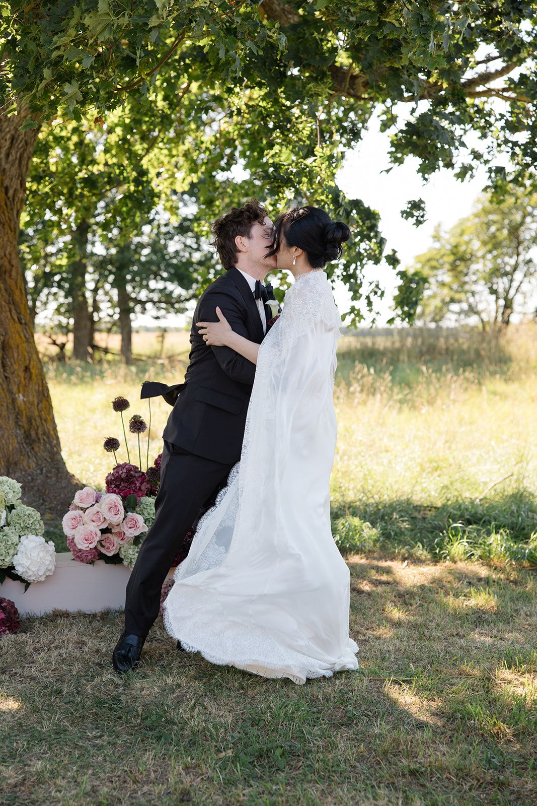 Romantic wedding couple shares intimate moments under a shady tree in a golden summer field.