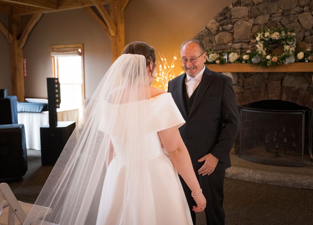 First look moment in front of stone fireplace in rustic timber frame venue.