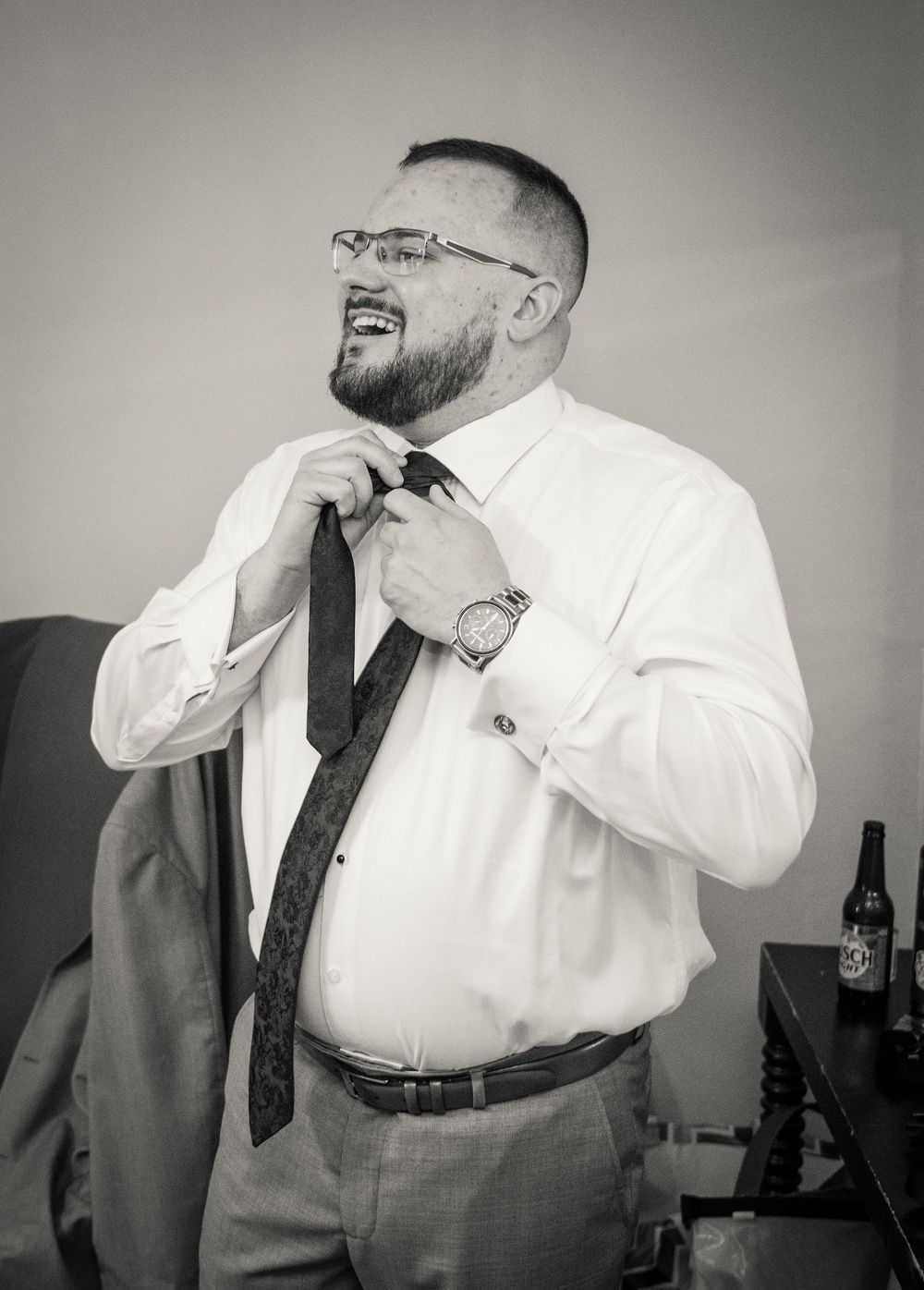 Black and white portrait of person adjusting tie while getting ready for formal event.
