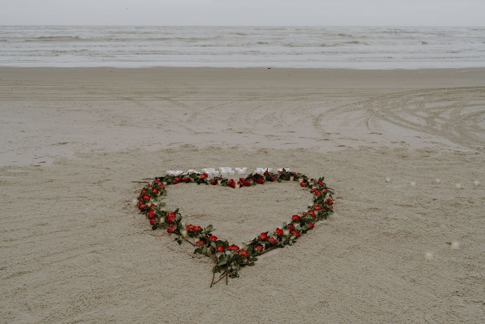 Rose petals arranged in a heart shape on sandy beach.