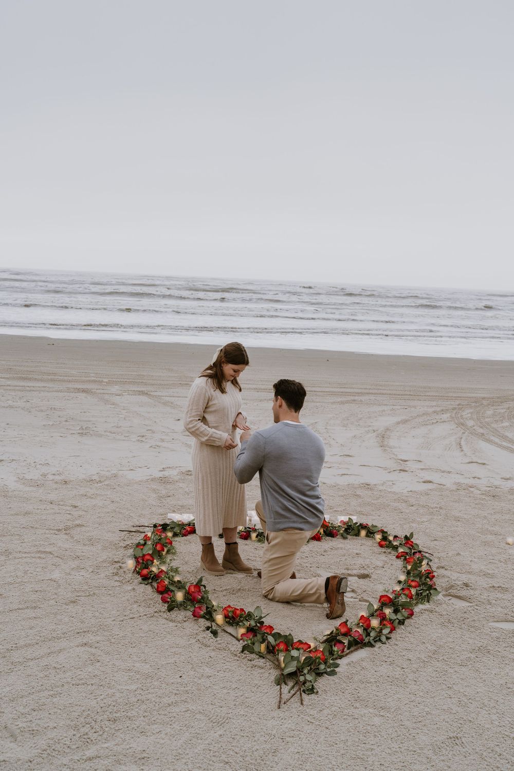 A romantic beach proposal with a heart made of flowers on the sand.