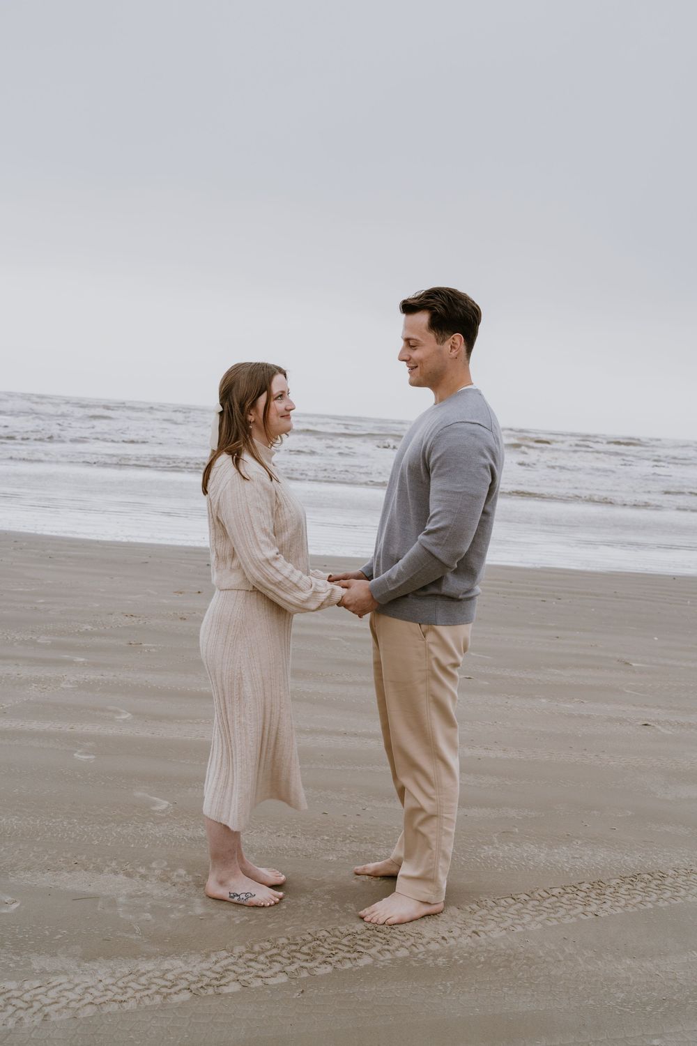 Two people stand barefoot on a beach holding hands during an intimate moment.