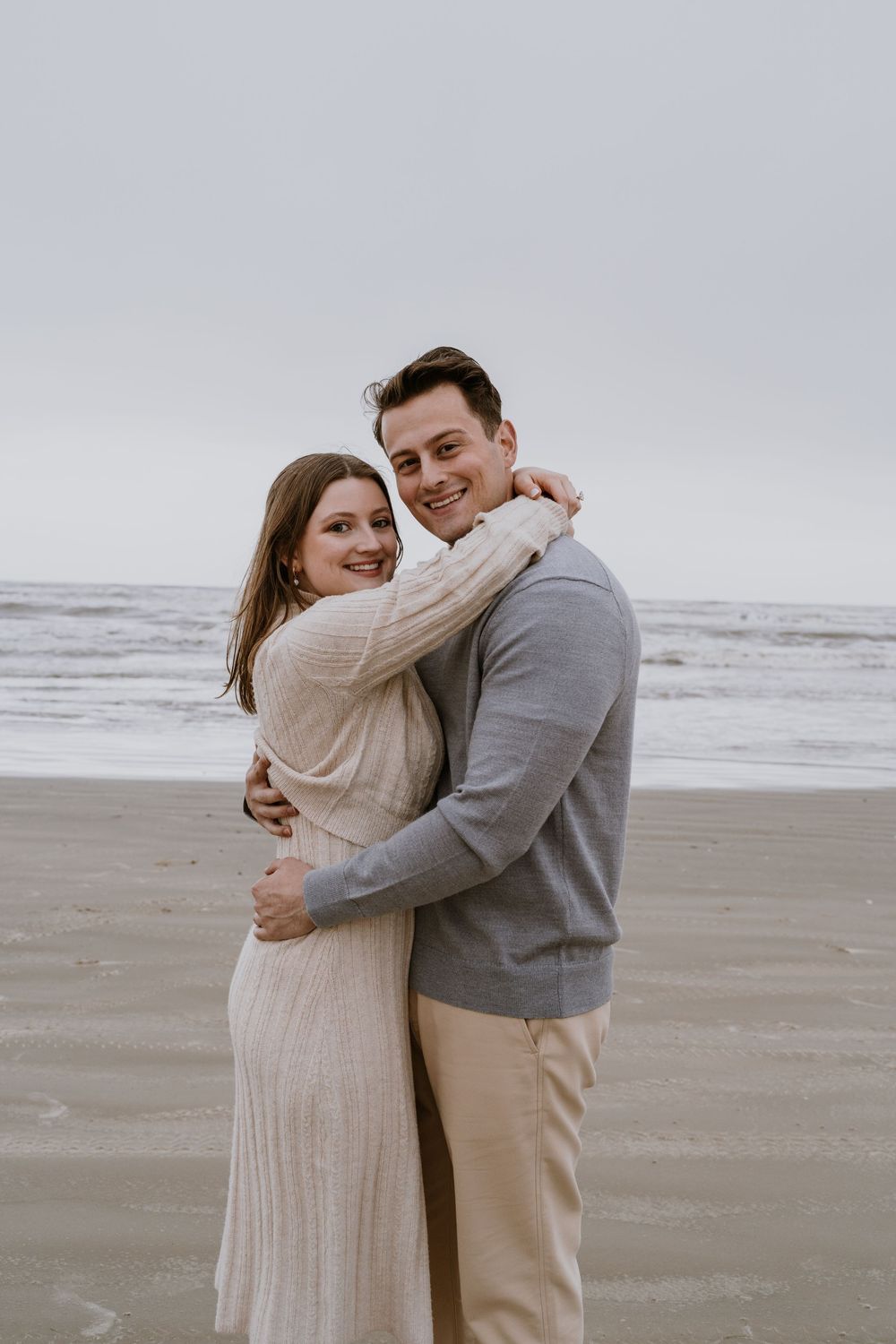 A happy couple embraces on the beach after their engagement.