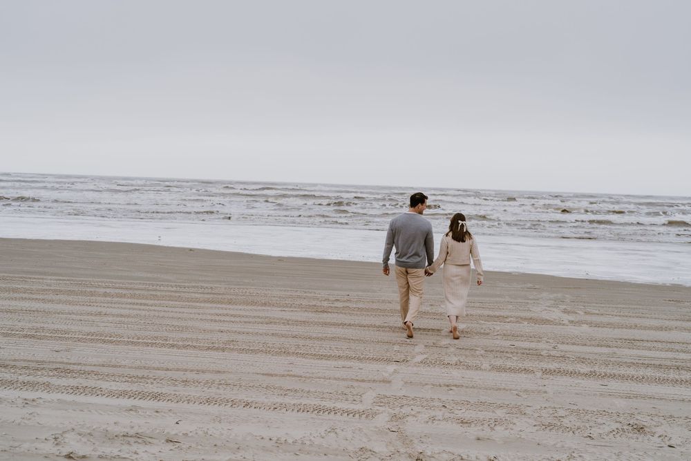 A couple walks along the beach together after their proposal.