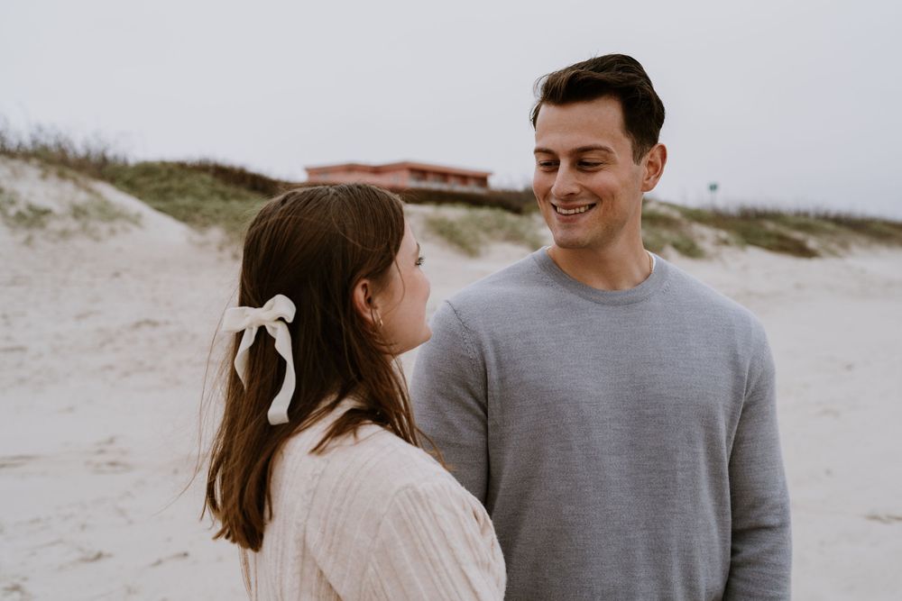 A couple in casual sweaters enjoys a tender moment at the beach.