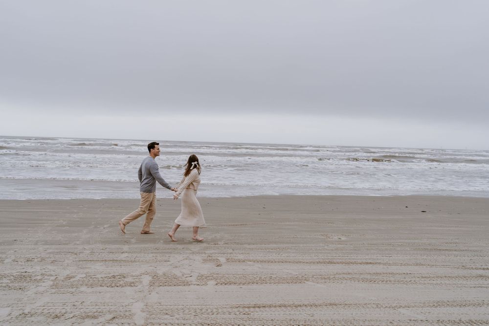 Two people walk together on an empty beach with waves in the distance.