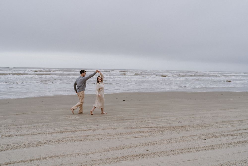 A couple strolls along a wide, empty beach on an overcast day.