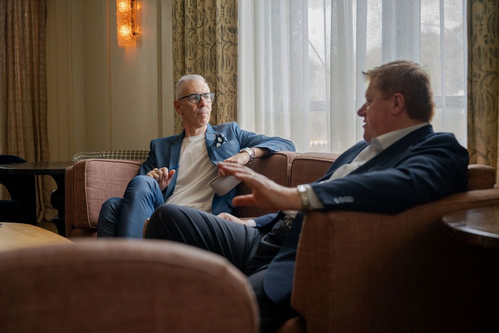 Two people having an engaged conversation while sitting comfortably in leather armchairs at an upscale venue.
