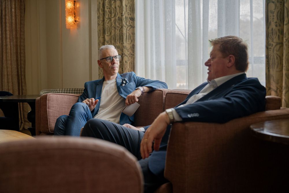 Two individuals engaged in animated discussion while relaxing in leather chairs at an elegant lounge.