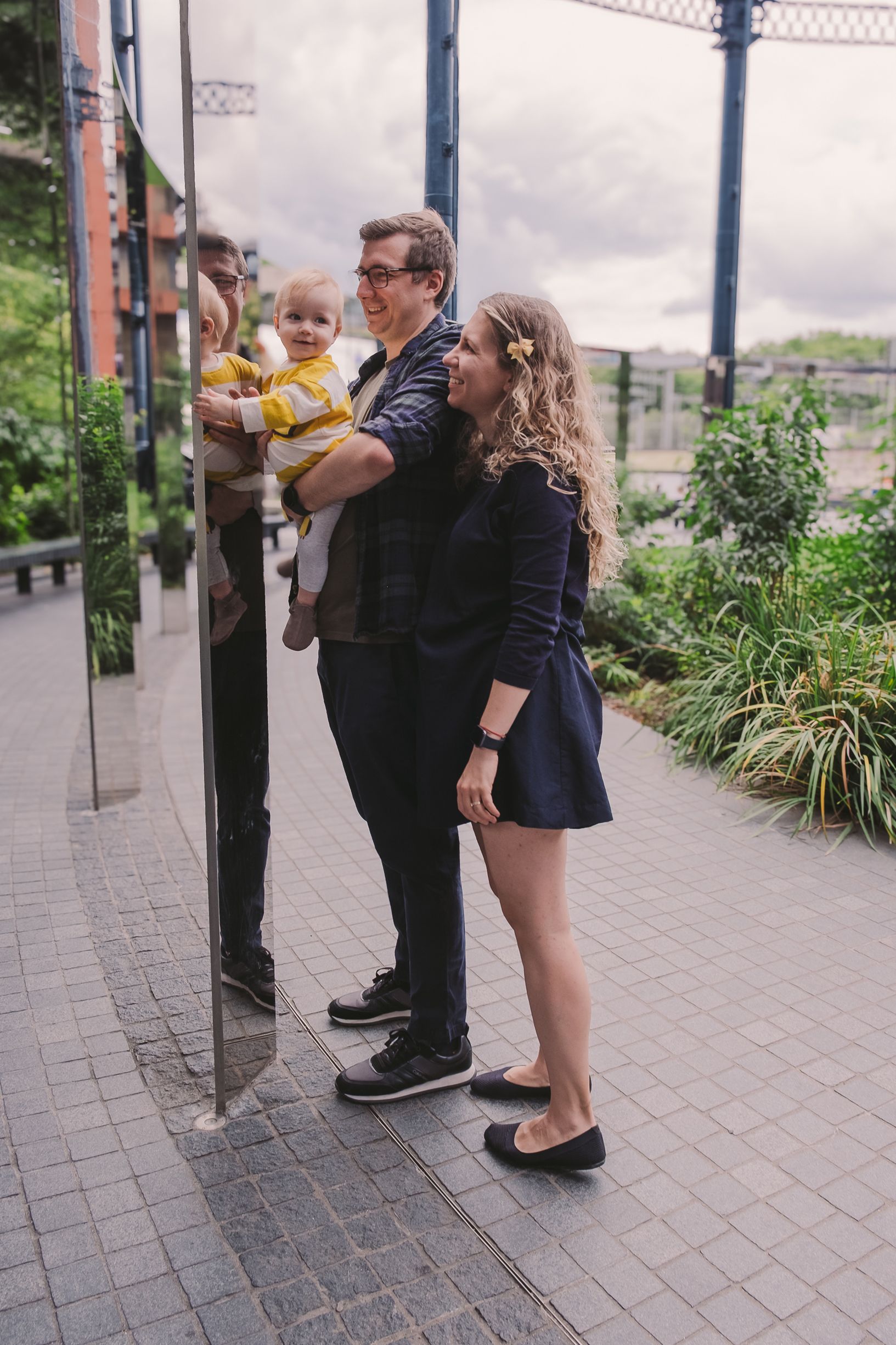 People standing together on a paved walkway with greenery and buildings visible in the background.