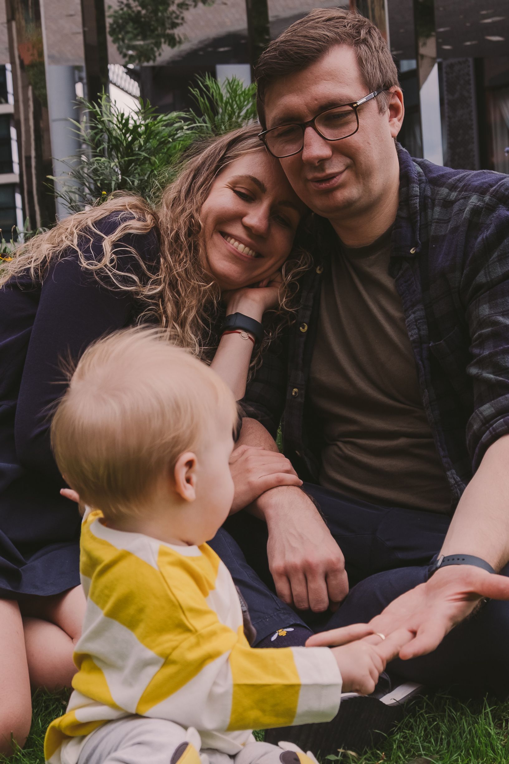 Intimate family moments captured while sitting on grass with urban scenery in background.